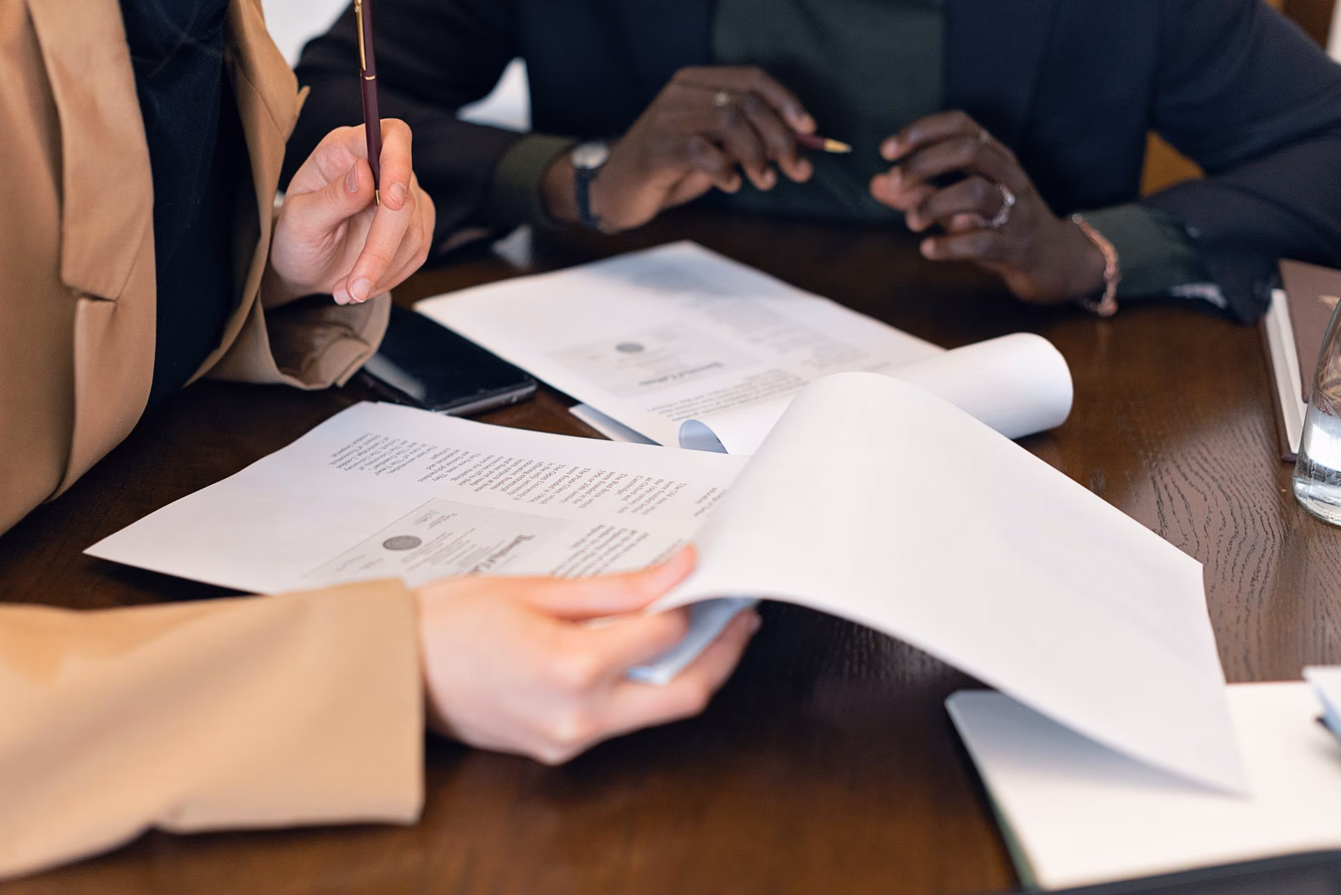 Two people reviewing and discussing printed documents at a wooden table during a meeting.