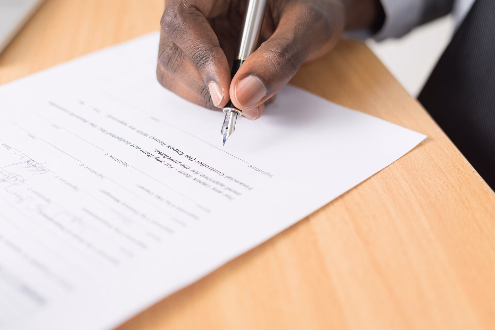Hand holding a fountain pen poised to sign a document on a wooden table.
