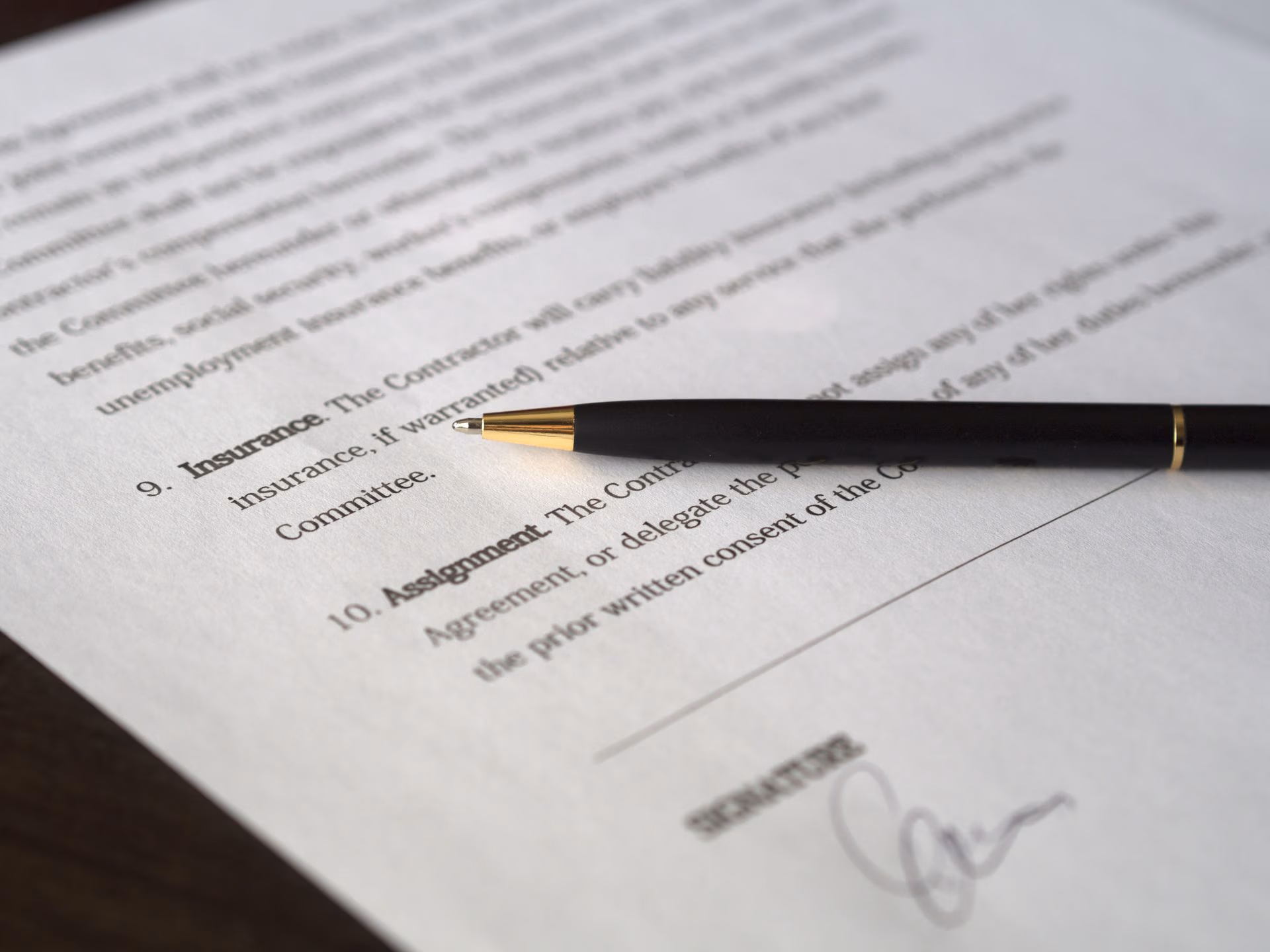 Black pen resting on a contract paper showing sections on Insurance and Assignment near a signature line.