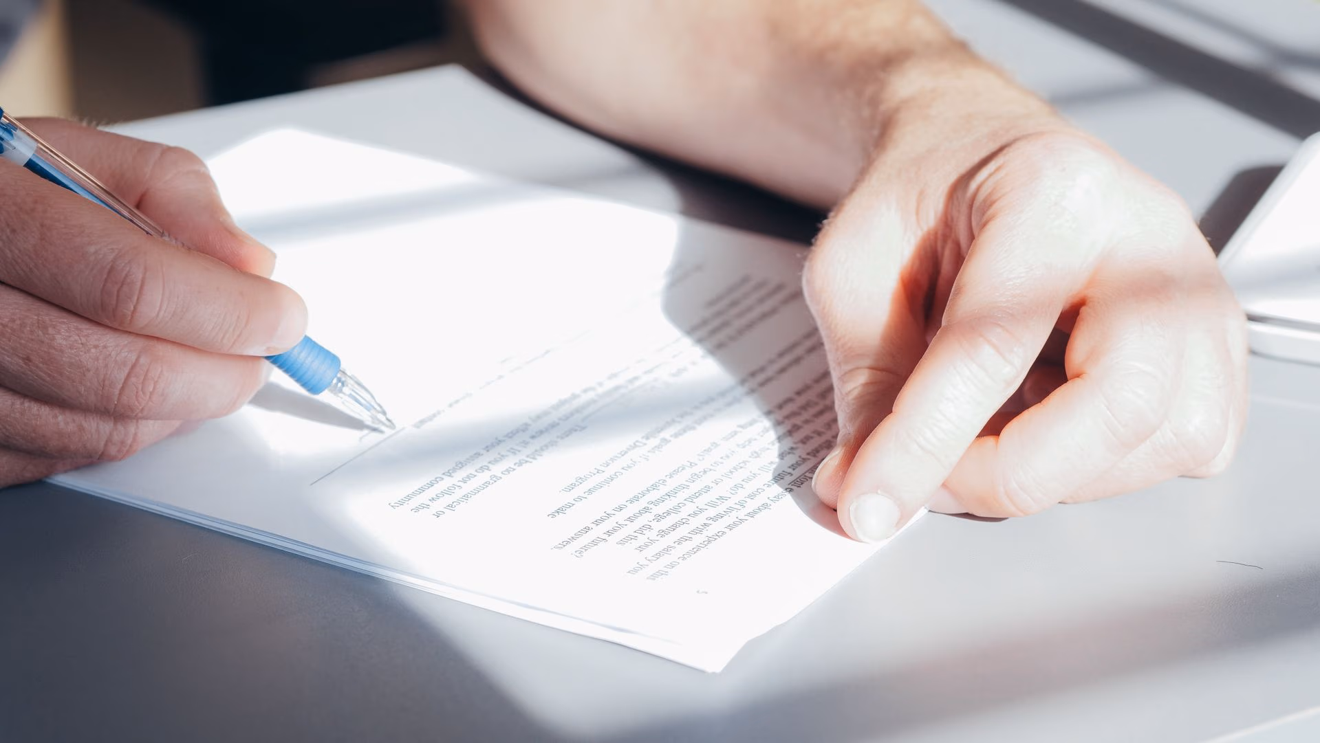 Close-up of hands signing a document with a blue pen on a white table.
