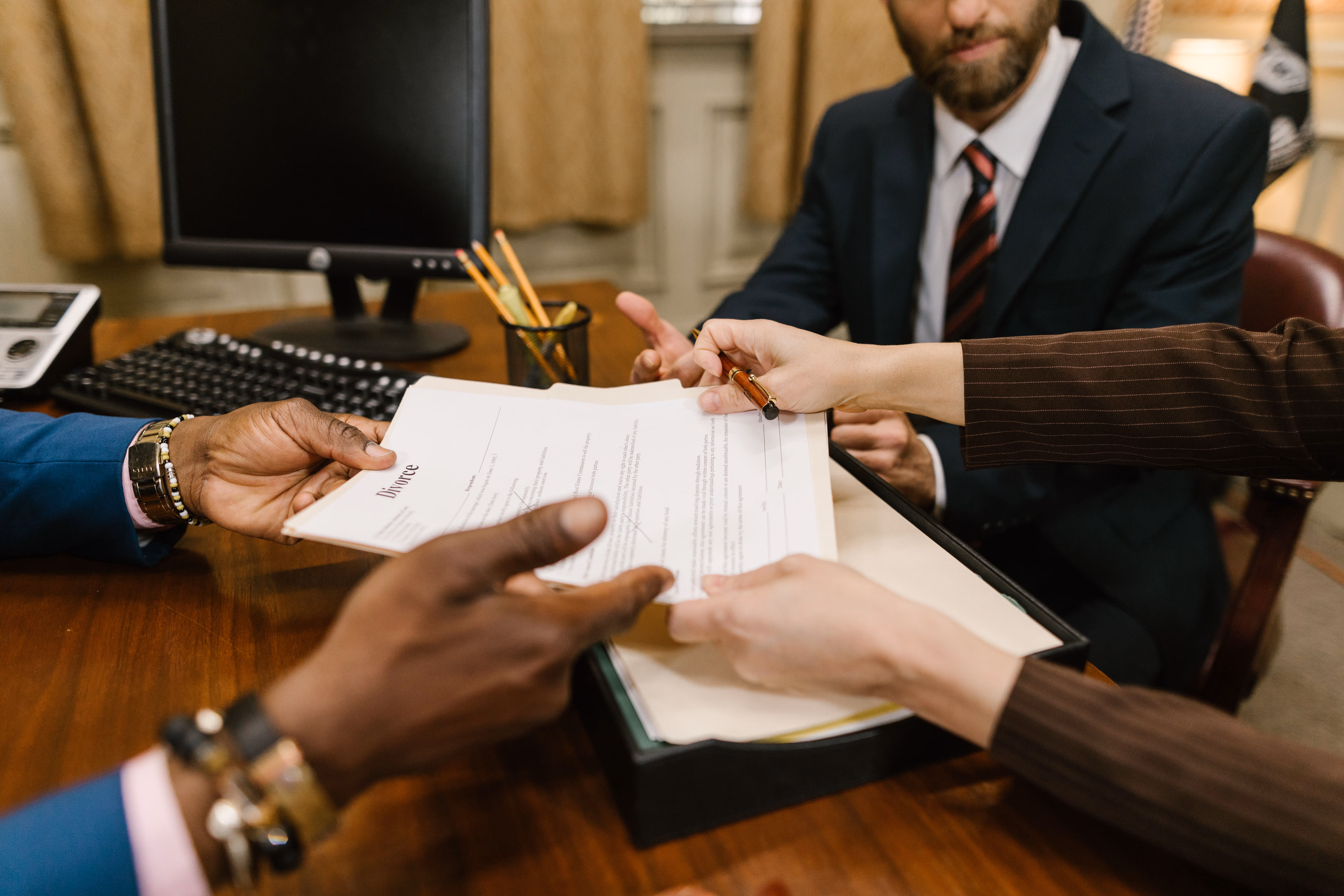Hands exchanging a divorce document over a desk with a man in a suit in the background.