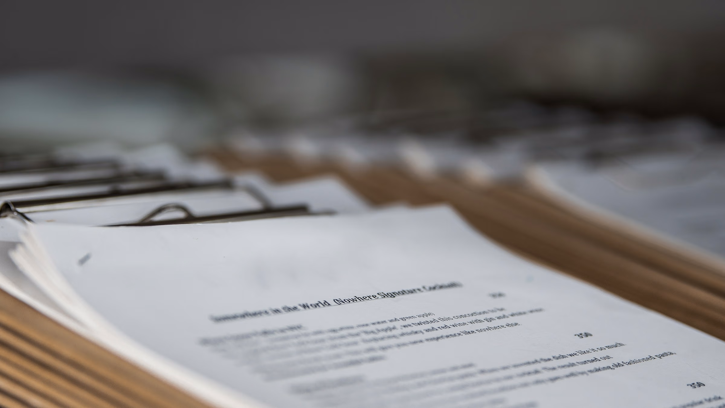 Stack of printed documents clipped with metal binders on a wooden surface.