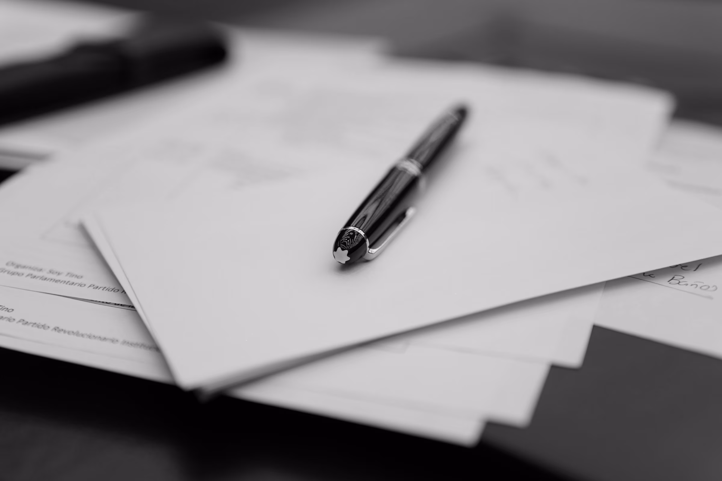 Black pen resting on a stack of scattered paperwork on a dark surface.