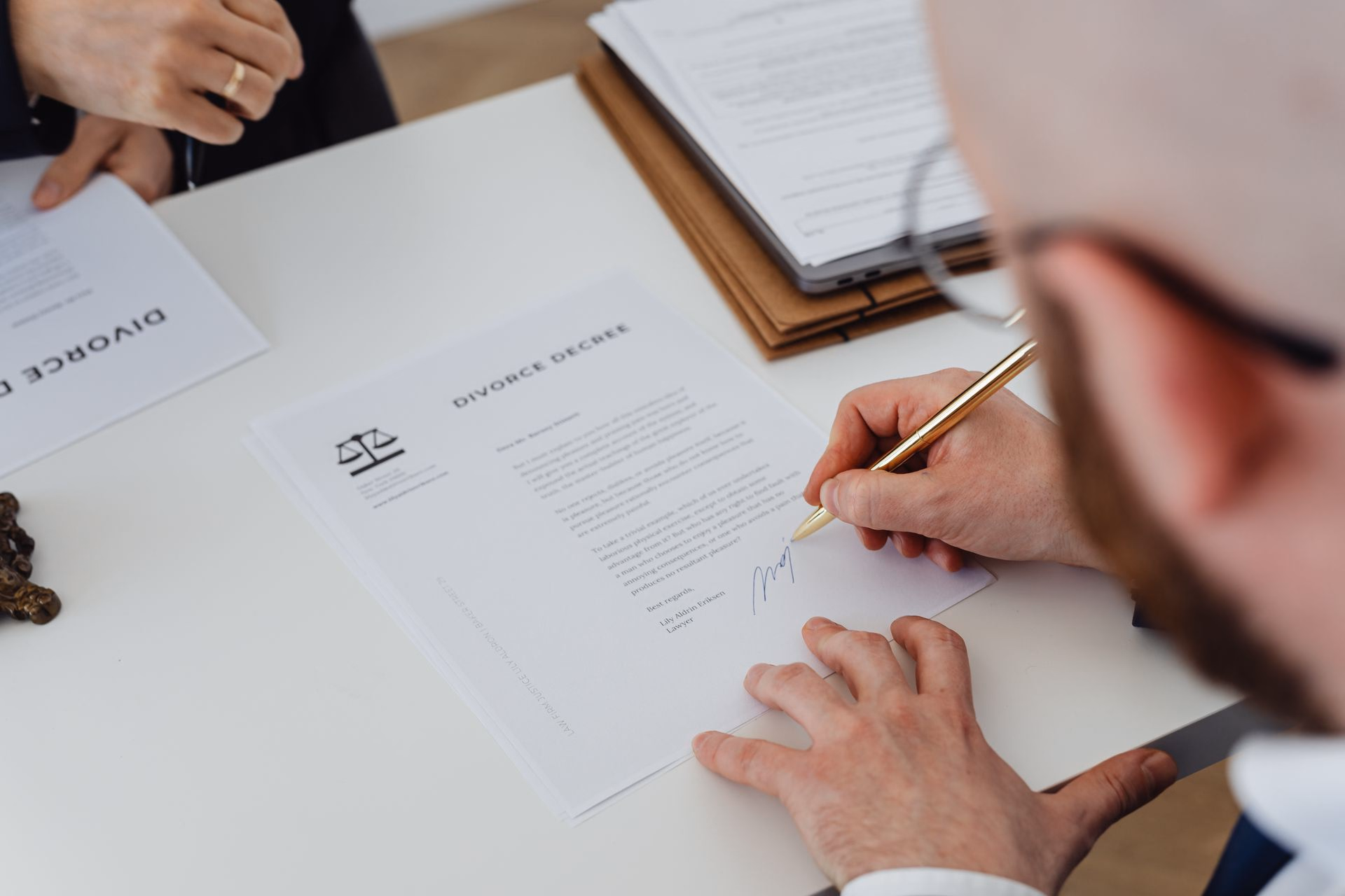 A man signing a document headed Divorce Decree with a gold pen at a white desk.