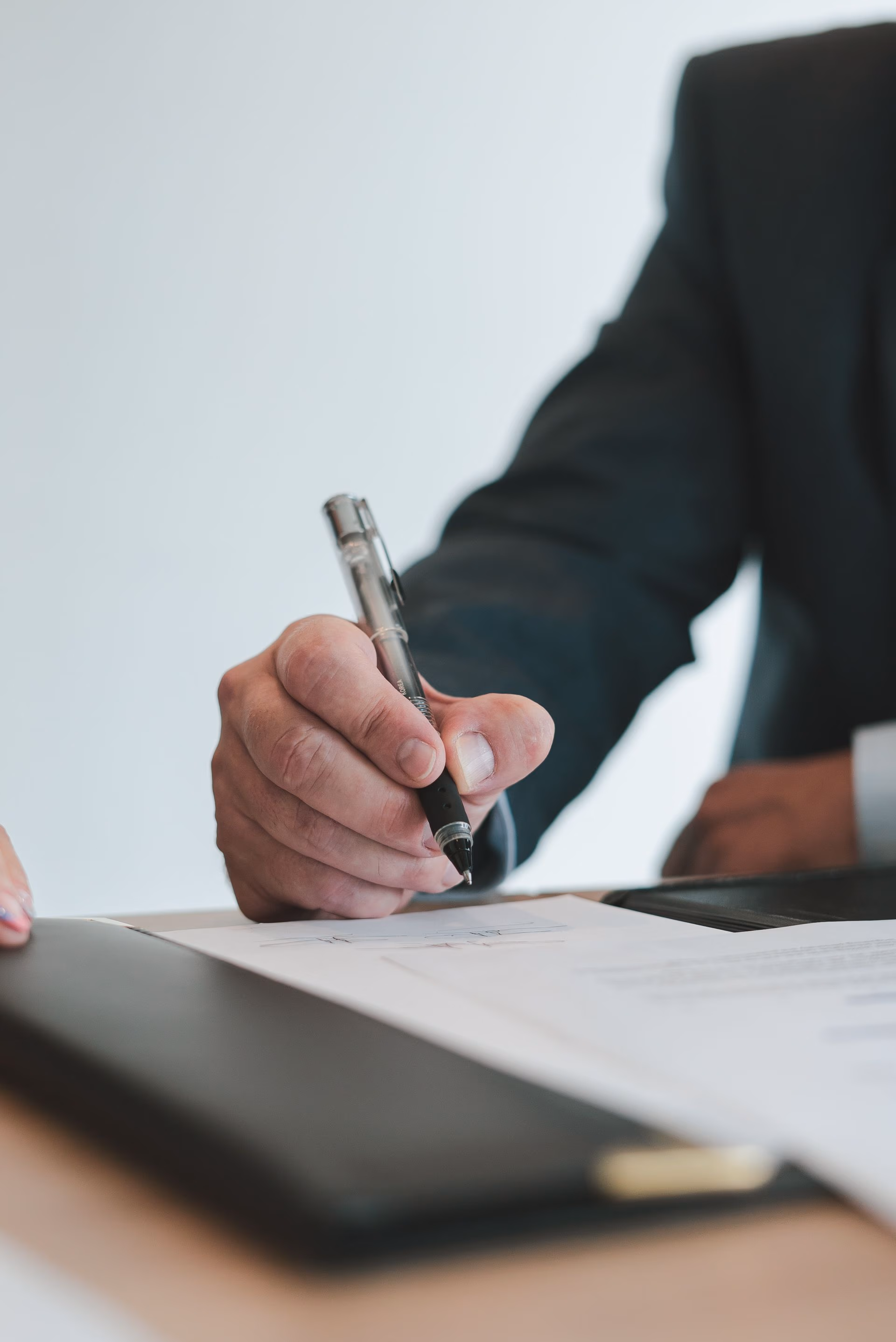 Close-up of a hand holding a pen poised to write on a document on a desk.